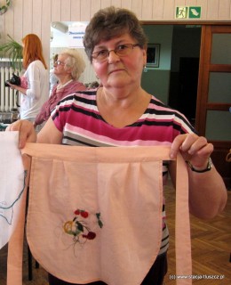 Wiesława Jędrysiak, która napisała projekt i zdobyła dofinansowanie na warsztaty haftu prezentuje fartuszek, nad którym pracuje jedna z uczestniczek